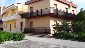 Un edificio residencial de dos pisos con balcones, una antena parabólica y un pequeño jardín con flores rosas.