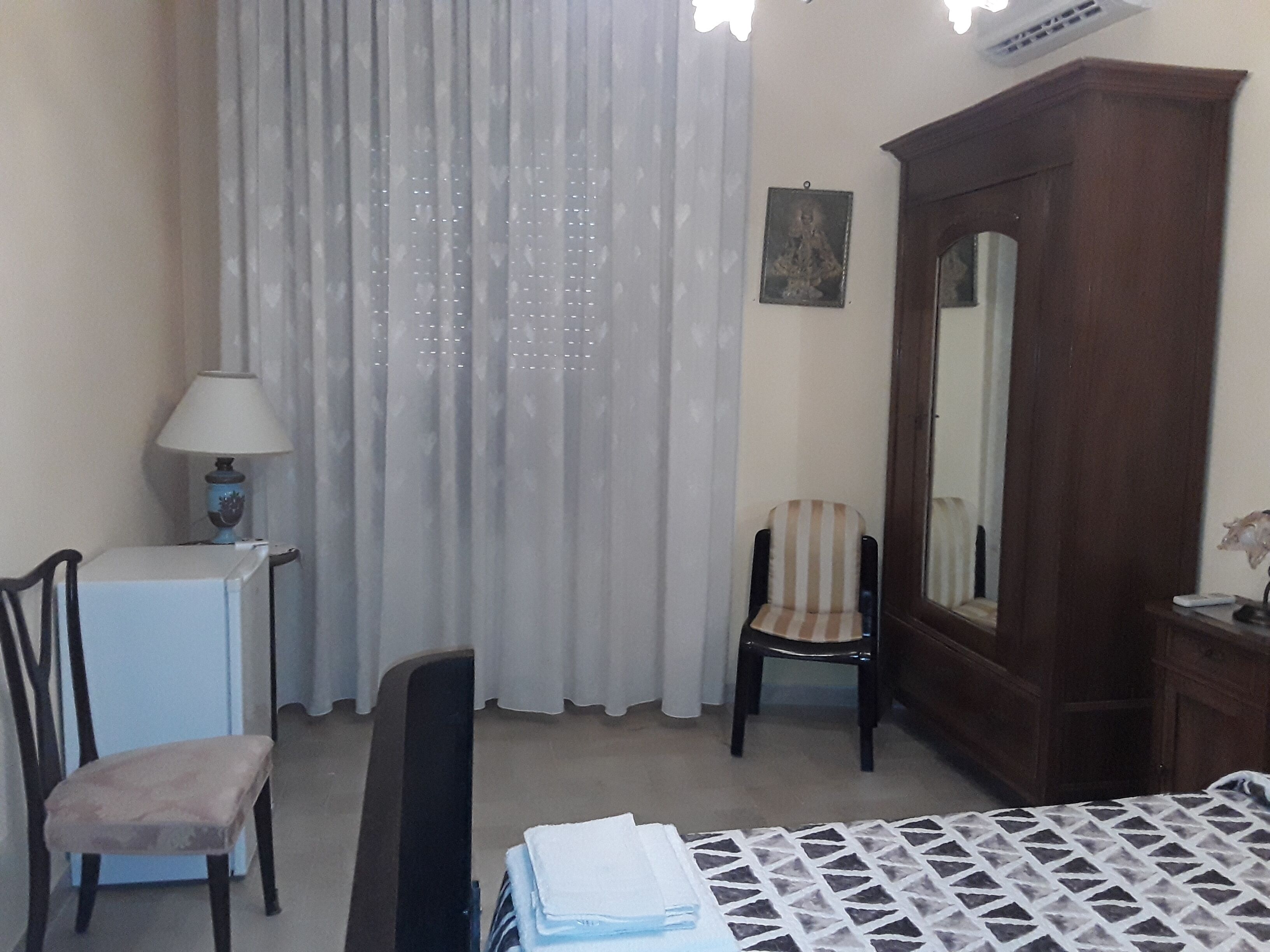 Ein Hotelzimmer mit Bett, Schreibtisch, Stuhl, Kleiderschrank und einem Fenster mit Vorhängen.
