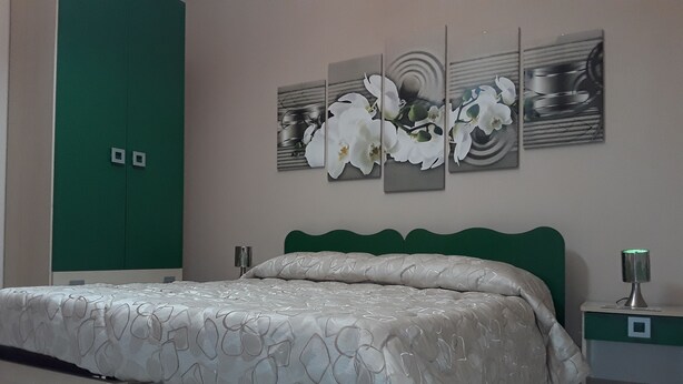 Un dormitorio con cama, cabecera verde, mesitas de noche y una pared con un cuadro floral.