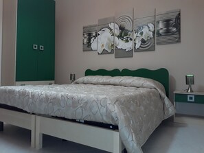 A bedroom with a bed, green headboard, nightstands, and a wall with a floral painting. - Elimo Affittacamere di Scardino Leonardo (Poggioreale)