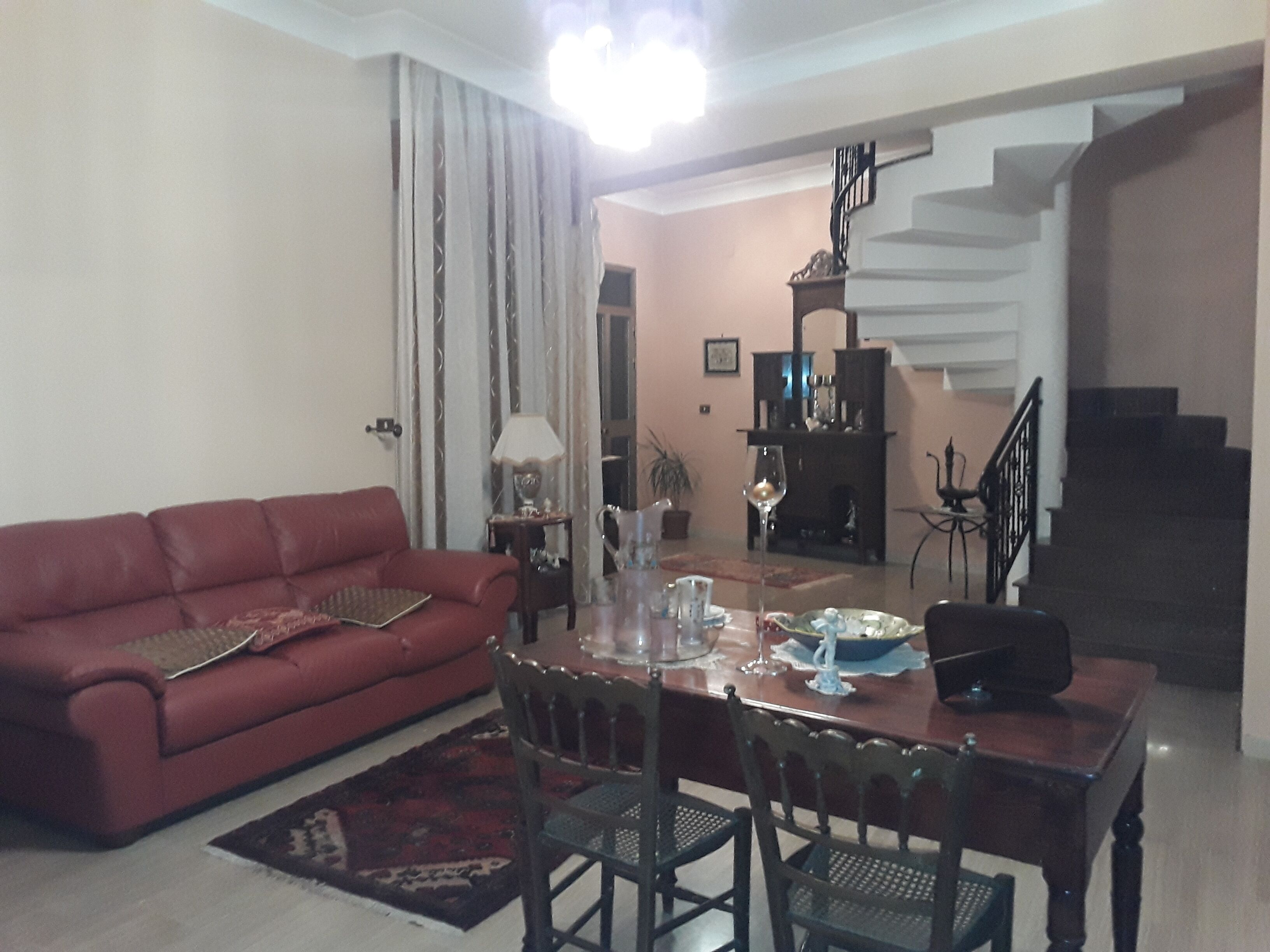 A living room with a red sofa, a dining table with chairs, a staircase, and a fireplace.