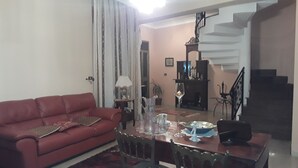 Una sala de estar con un sofá rojo, una mesa de comedor con sillas, una escalera y una chimenea.