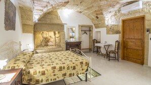 A bedroom with a stone ceiling, a bed with a patterned bedspread, a desk with a chair, and a wooden door. - Dimora Corte Antica Scorrano (Scorrano)