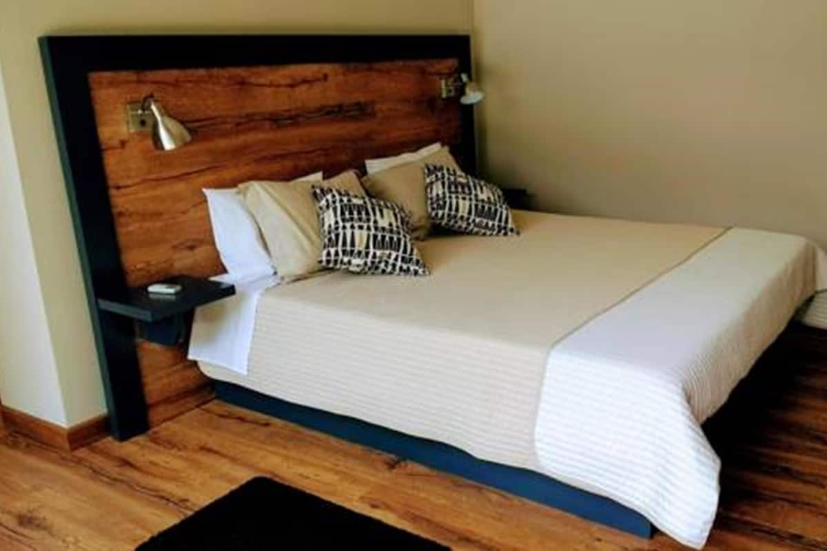 Un lit bien fait, avec une tête de lit en bois, du linge de lit blanc et des coussins à motifs.