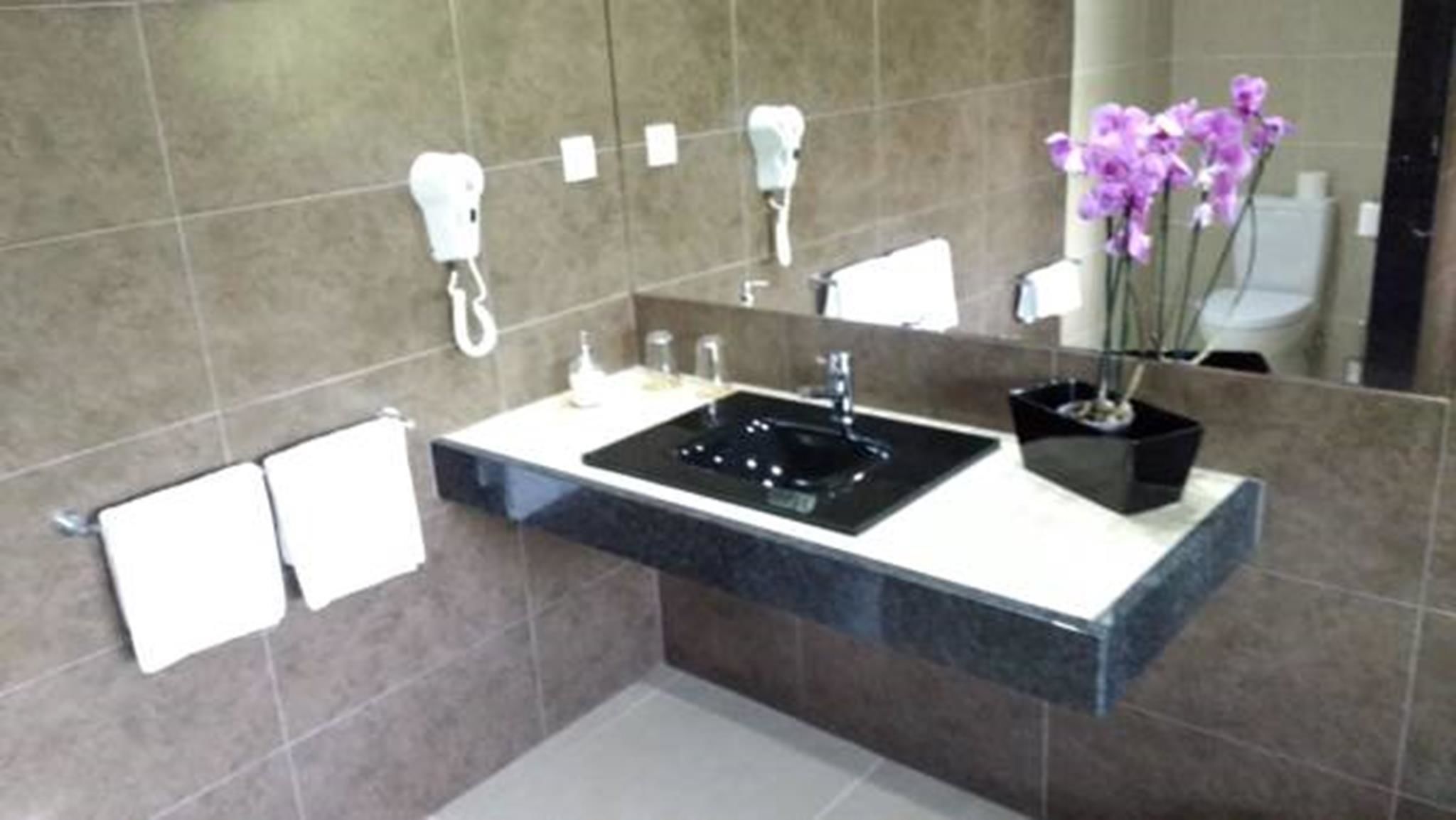 A modern bathroom with a black sink, white towel racks, and a potted orchid.