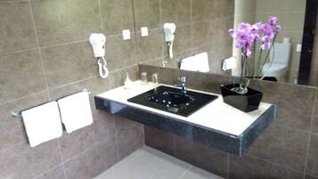 A modern bathroom with a black sink, white towel racks, and a potted orchid.