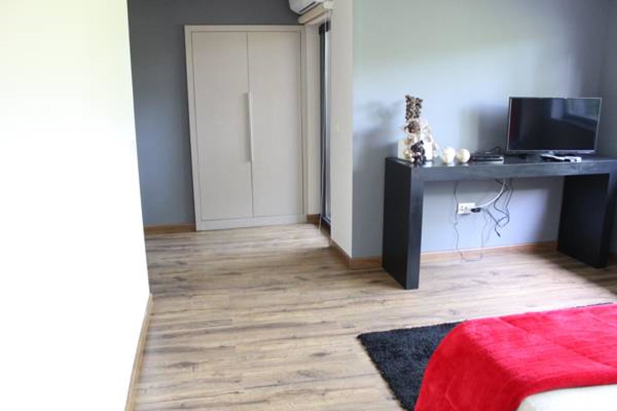 Un dormitorio con cama, escritorio con computadora, televisor y armario.