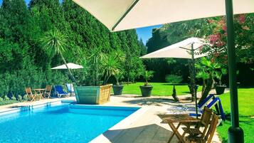 Una piscina al aire libre, sombrillas, sillones reclinables de piscina