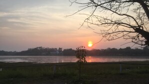 A sunset over a calm lake with a tree in the foreground and a fence along the water's edge. - SiBamboo 2 (Chiang Rai)