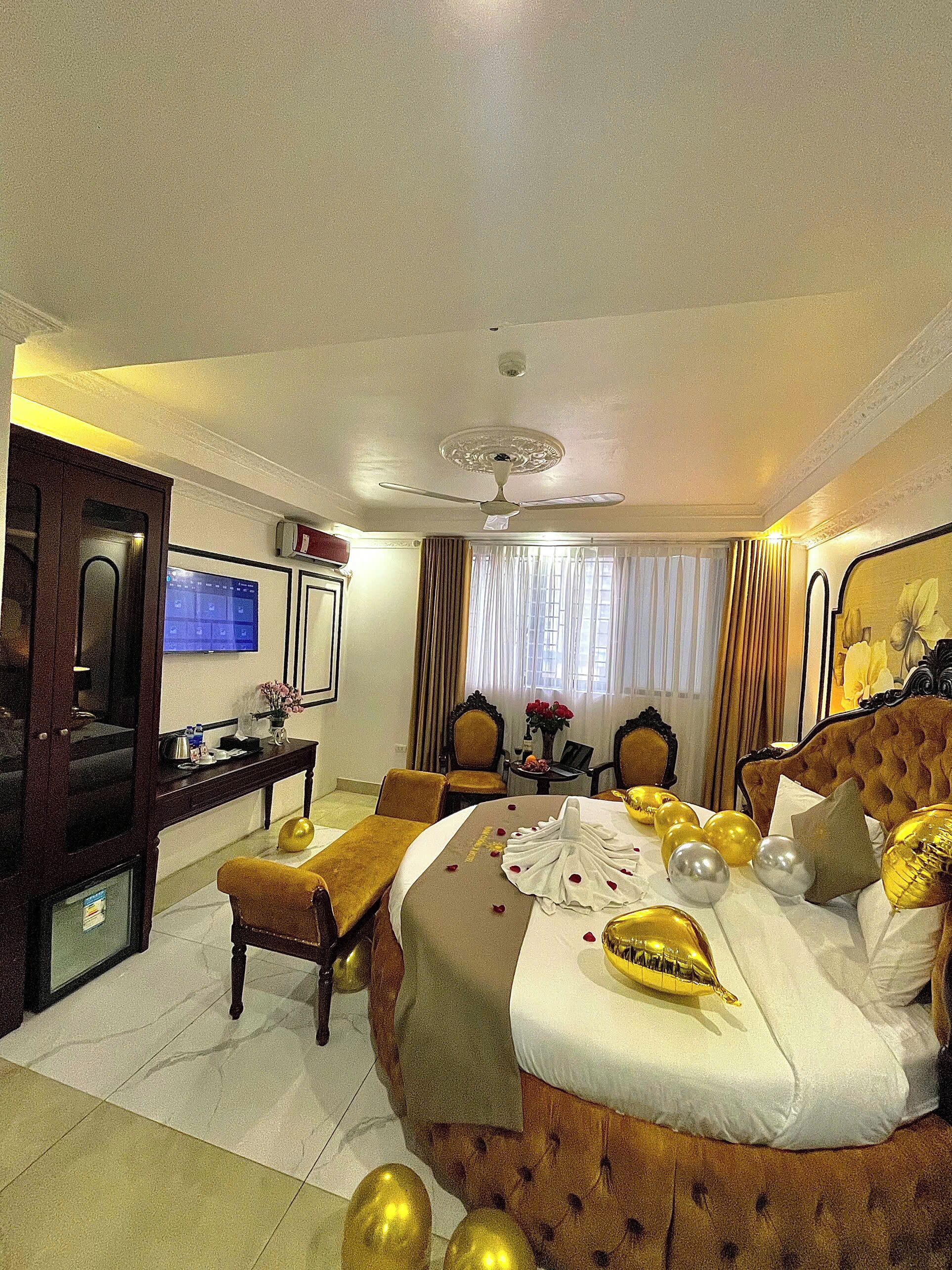 A hotel room with a large bed, a desk, a chair, a television, and a ceiling fan.