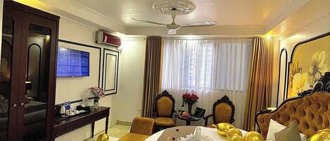 A hotel room with a large bed, a desk, a chair, a television, and a ceiling fan.