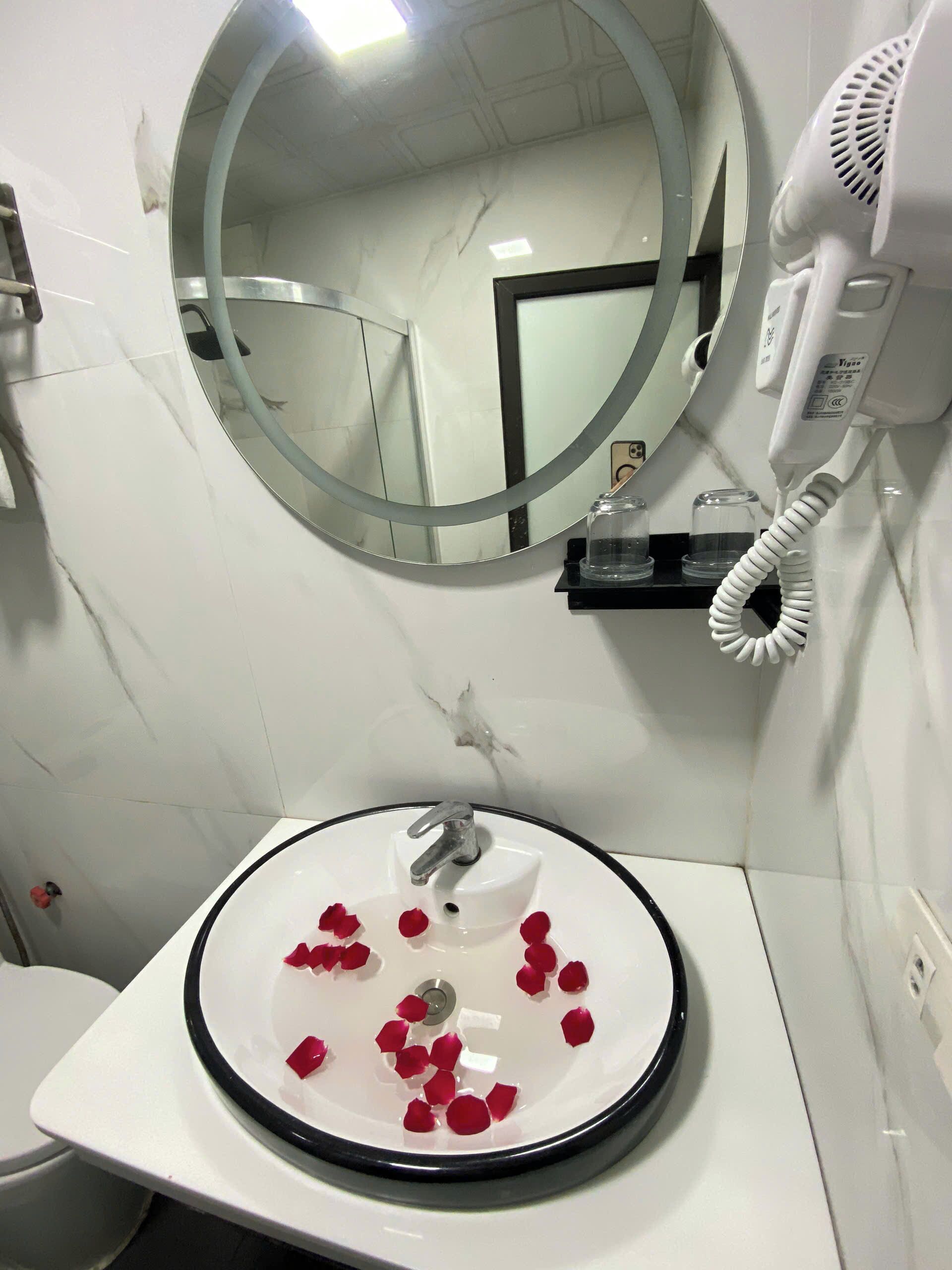 Ein Badezimmer mit einem runden Spiegel, einem Waschbecken mit Rosenblüten und einem Föhn an der Wand.