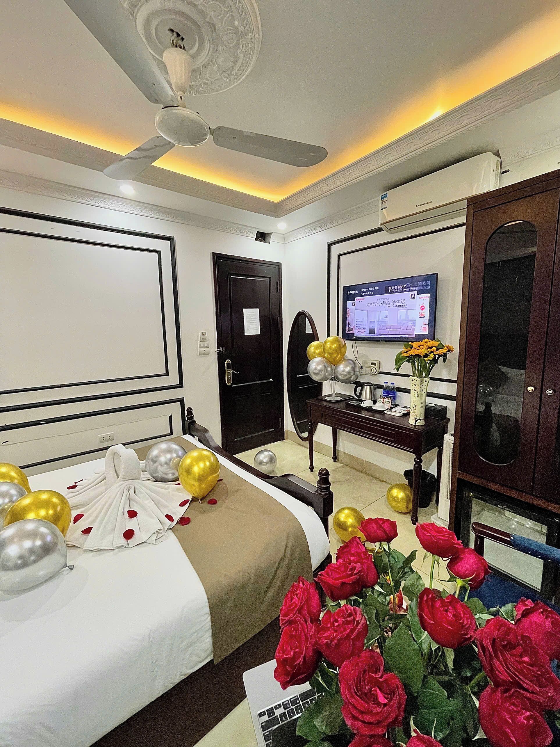 Una habitación de hotel con una cama, un escritorio con computadora, un televisor y un florero decorativo.