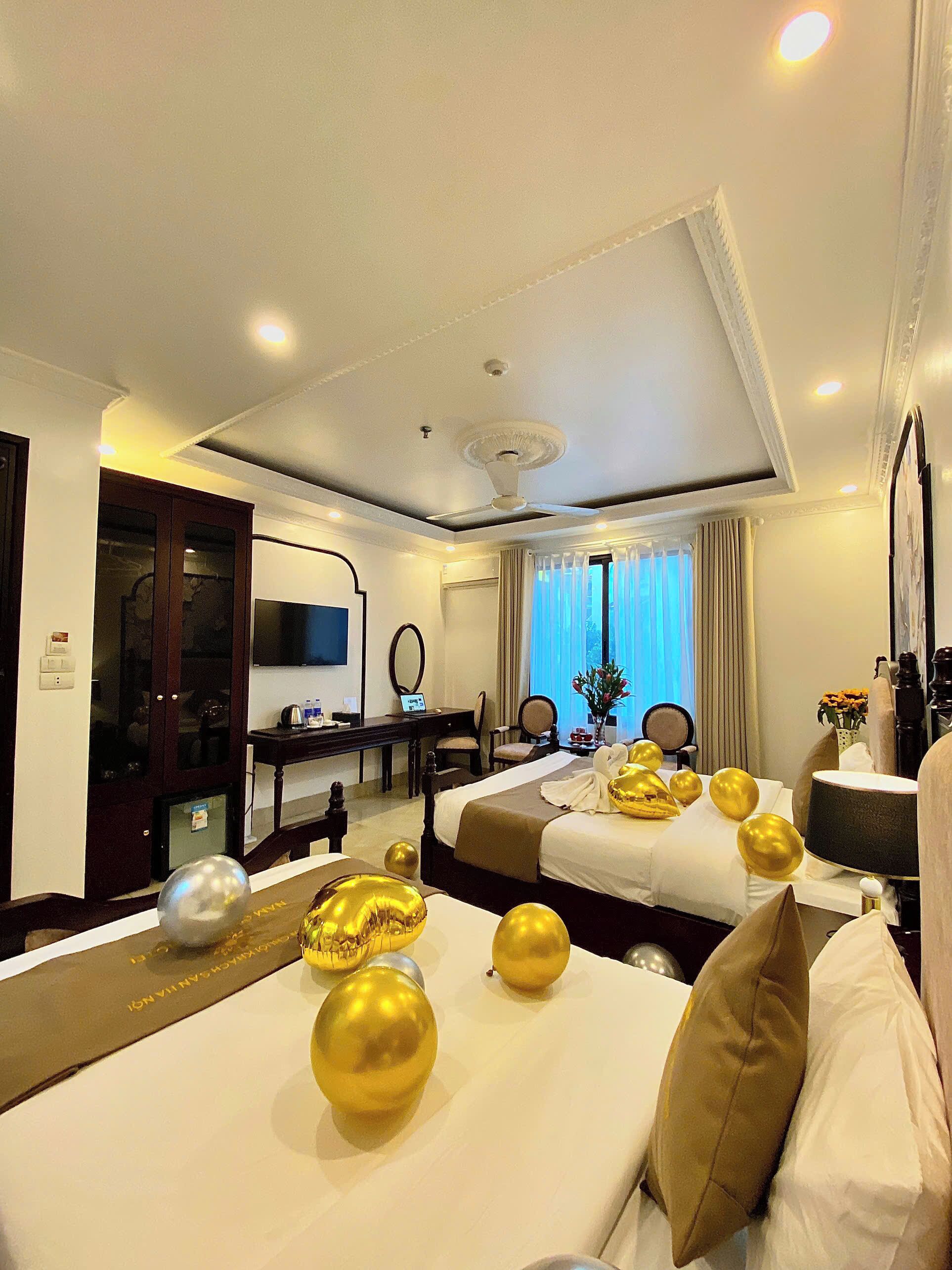 A hotel room with two beds, a desk, a TV, and a large window with curtains.