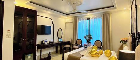 A hotel room with two beds, a desk, a TV, and a large window with curtains.