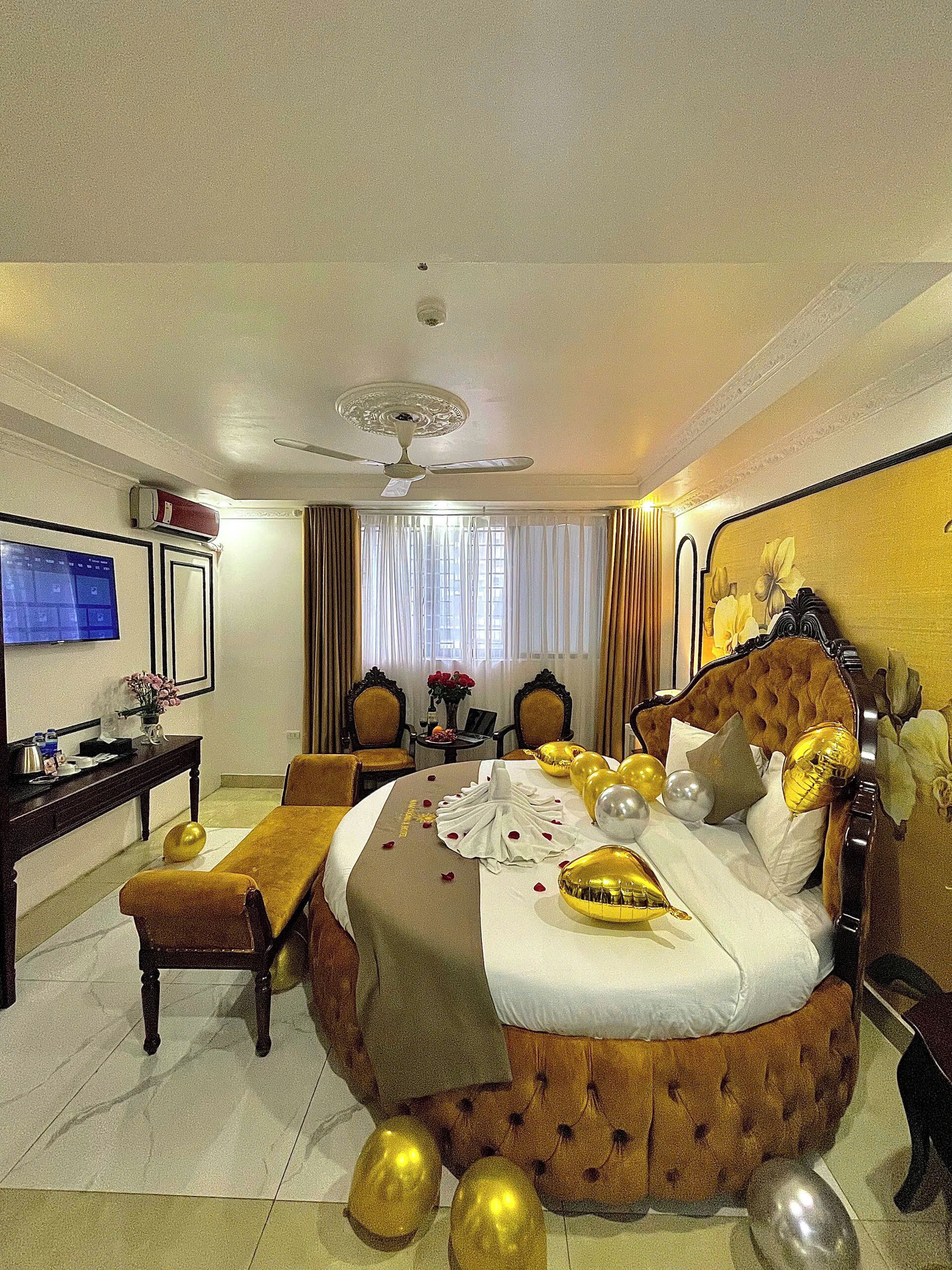 A hotel room with a round bed, a desk with a computer, a chair, a television, and a ceiling fan.