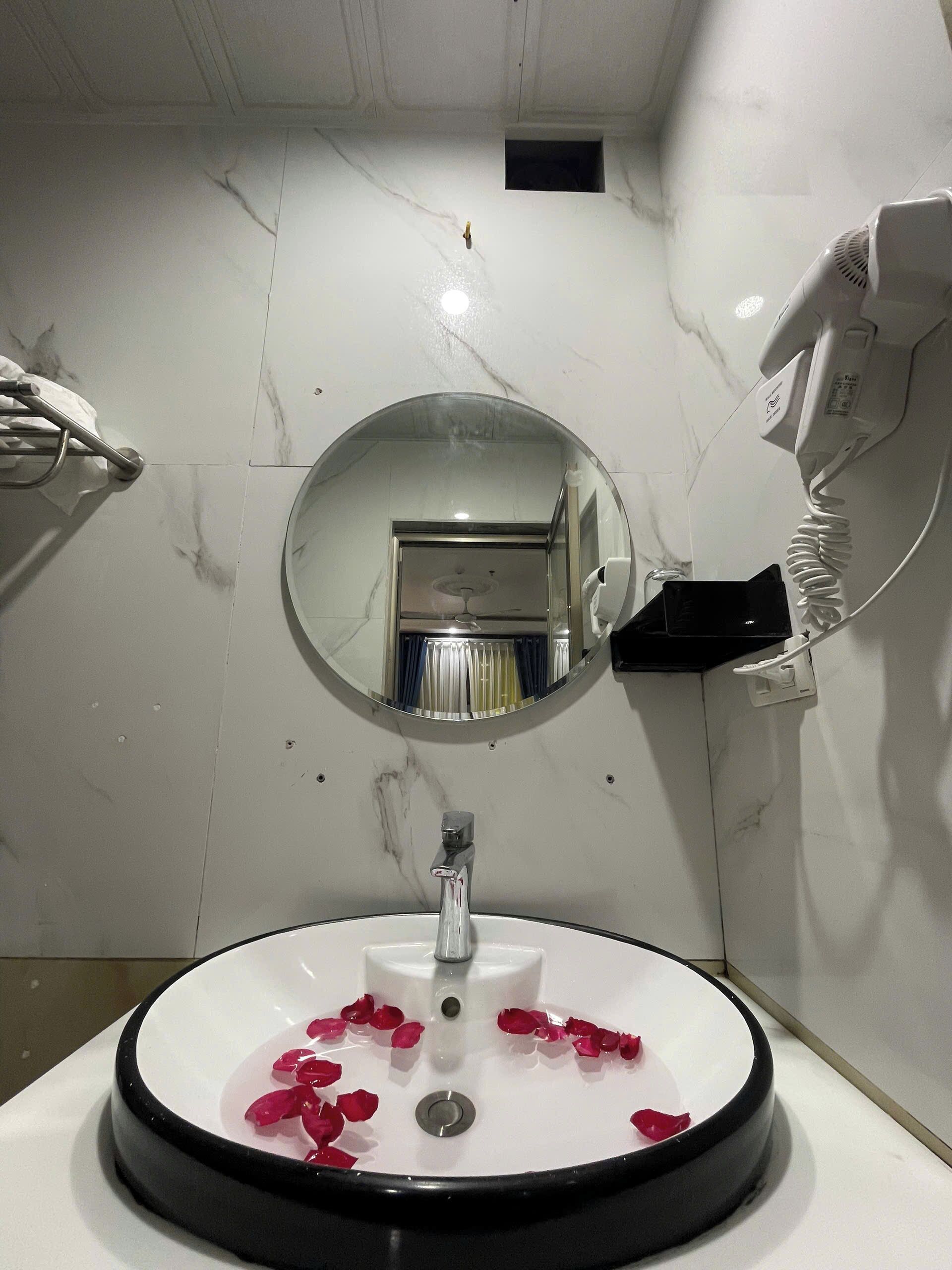 A bathroom with a white sink, a mirror, and a hairdryer mounted on the wall.