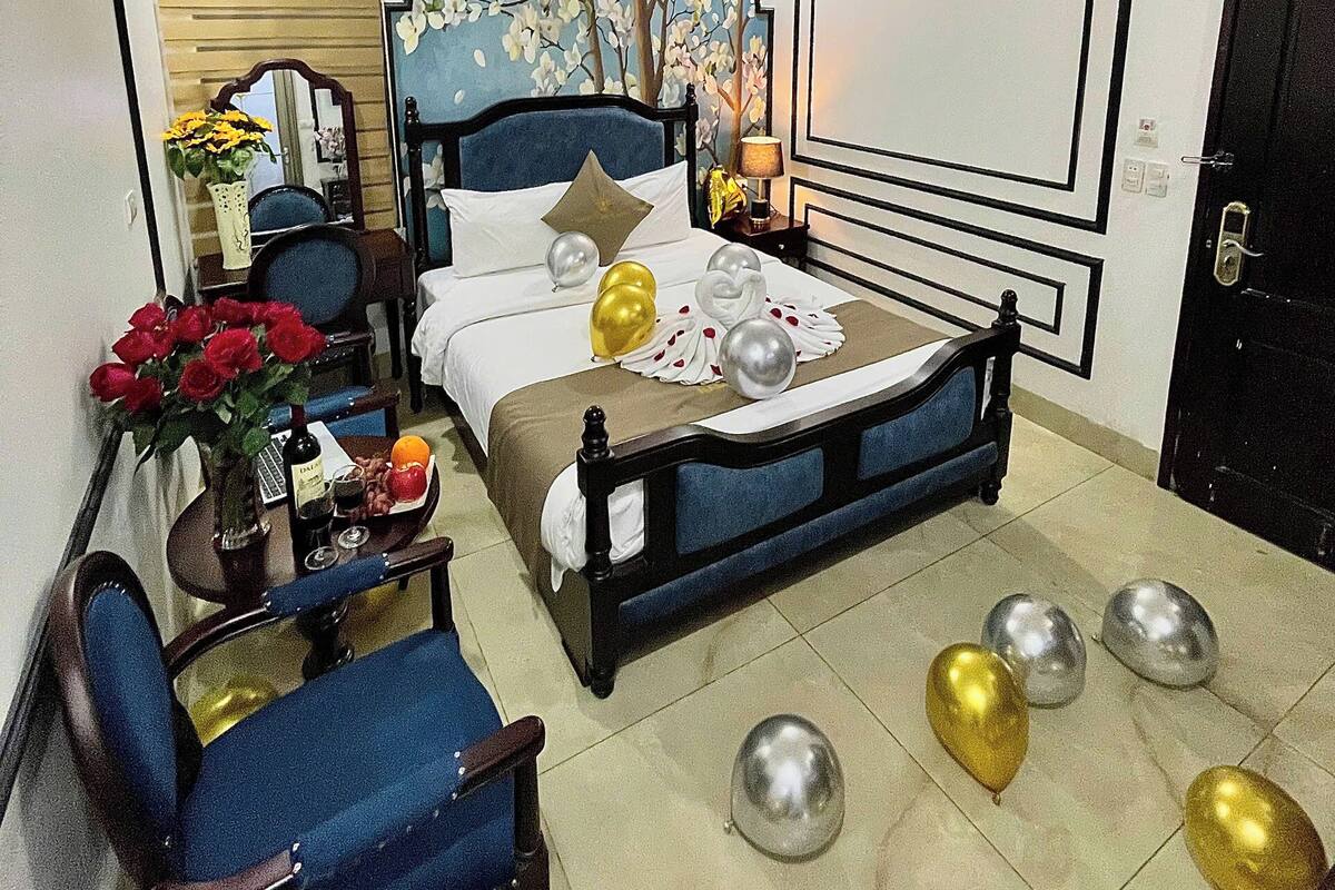 Une chambre avec un lit, une chaise, une table avec des fleurs et des ballons sur le sol.