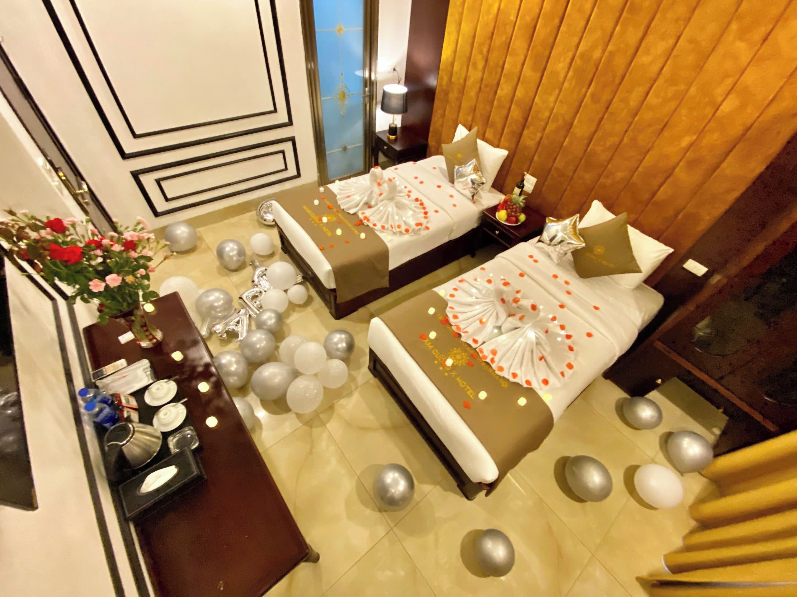 A hotel room with two beds, a minibar, a flower arrangement, and a view of the city.