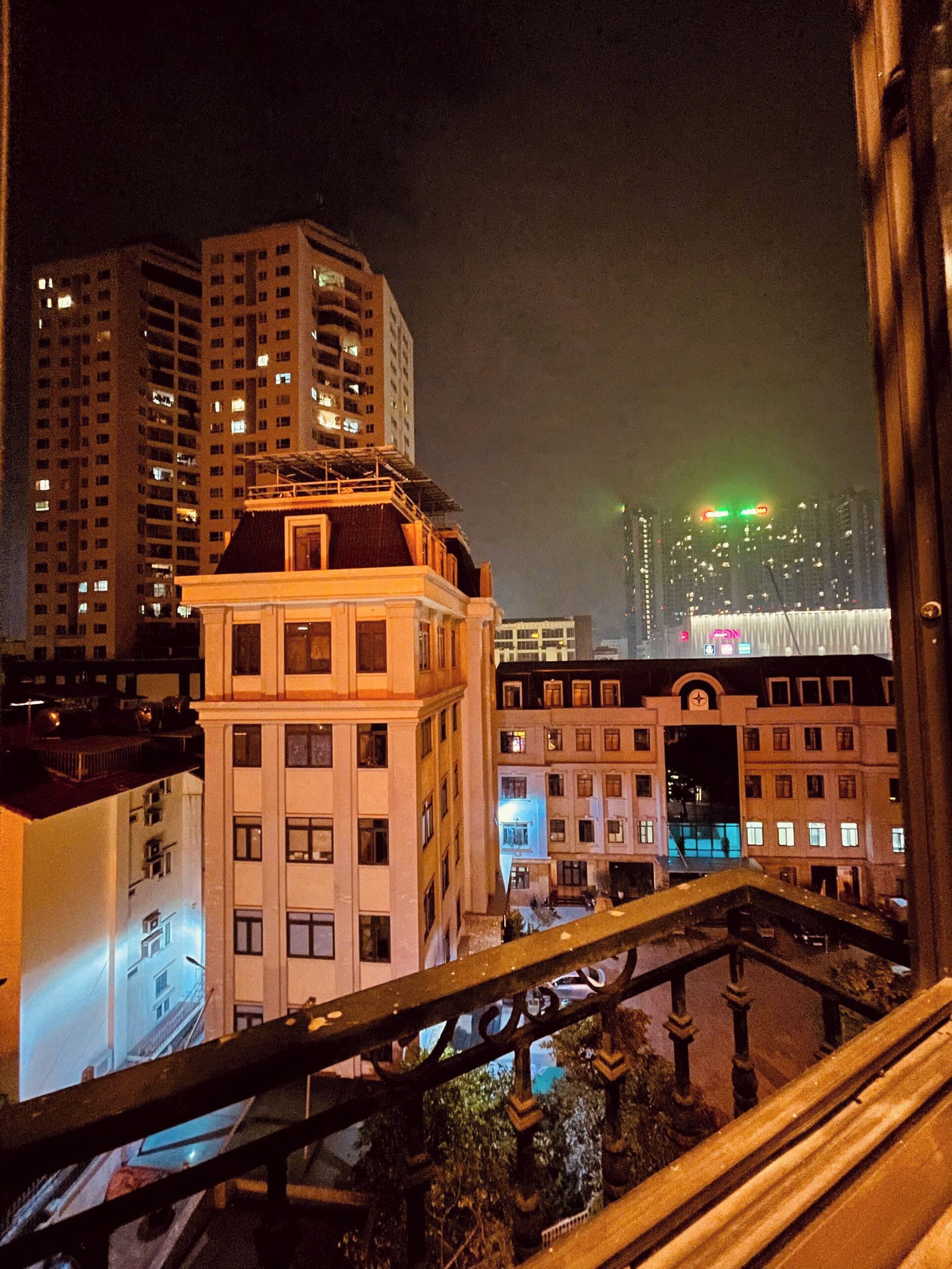 Paesaggio urbano notturno con grattacieli e un edificio in primo piano con un balcone.