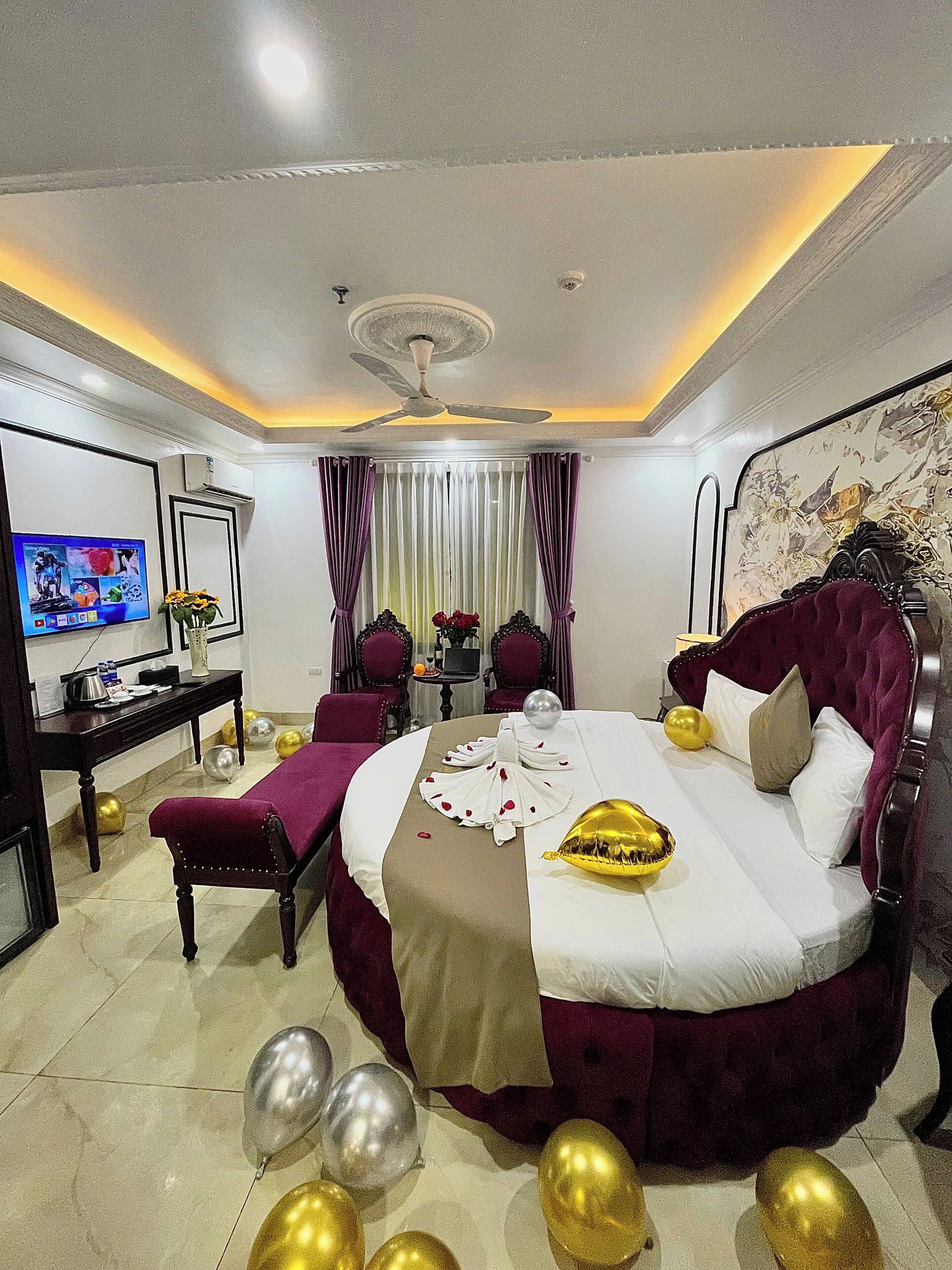 A hotel room with a large bed, a desk, a television, and a ceiling fan.