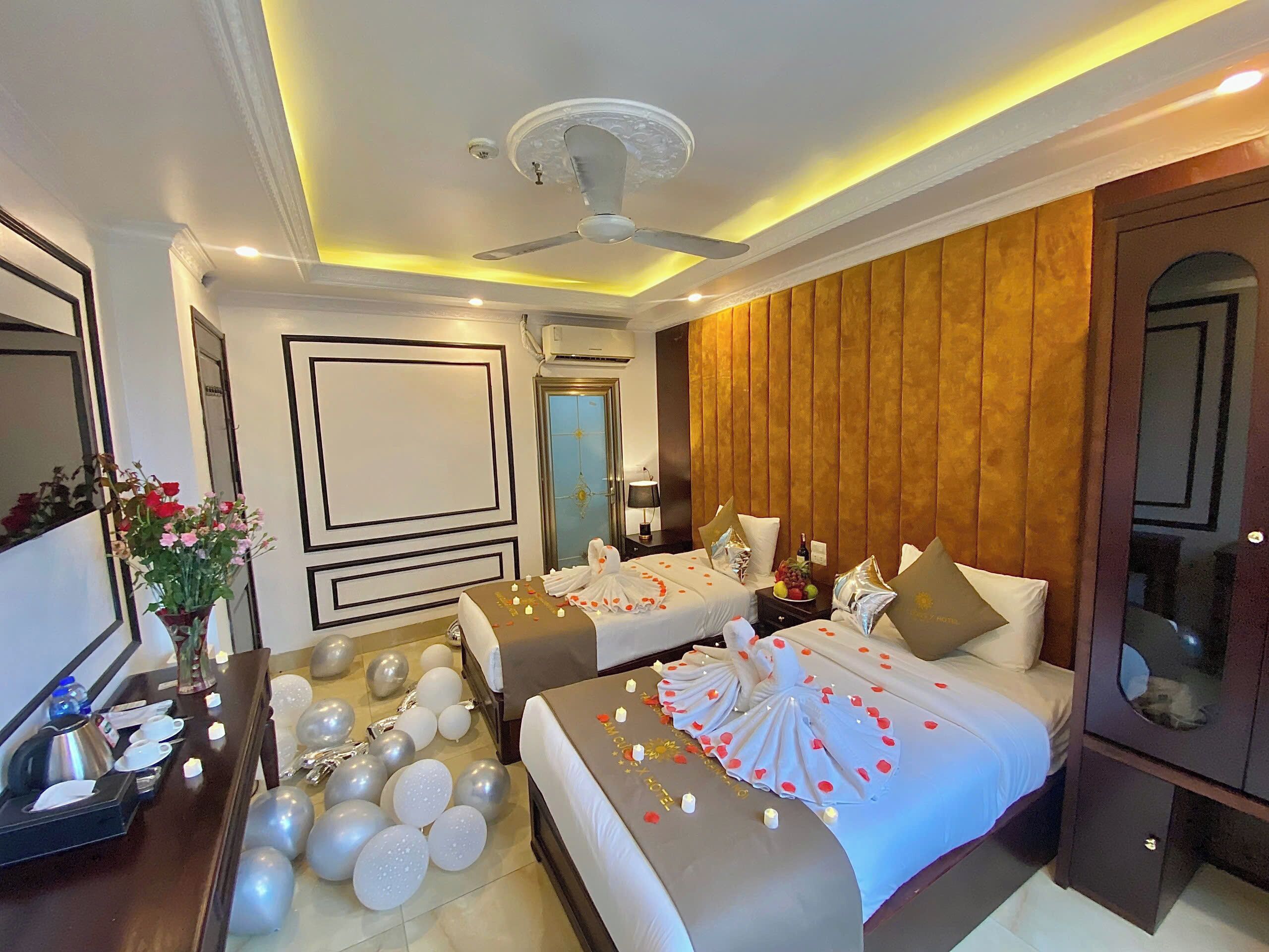A hotel room with two beds, a mirror, a vanity, and a decorative arrangement of balloons and flowers.