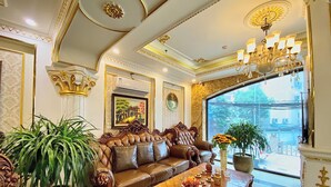 A luxurious living room with a large brown leather sofa, a wooden coffee table with decorative items, and a large window offering a view of the outdoors. - Nam Cuong X Hotel (Hanoi)