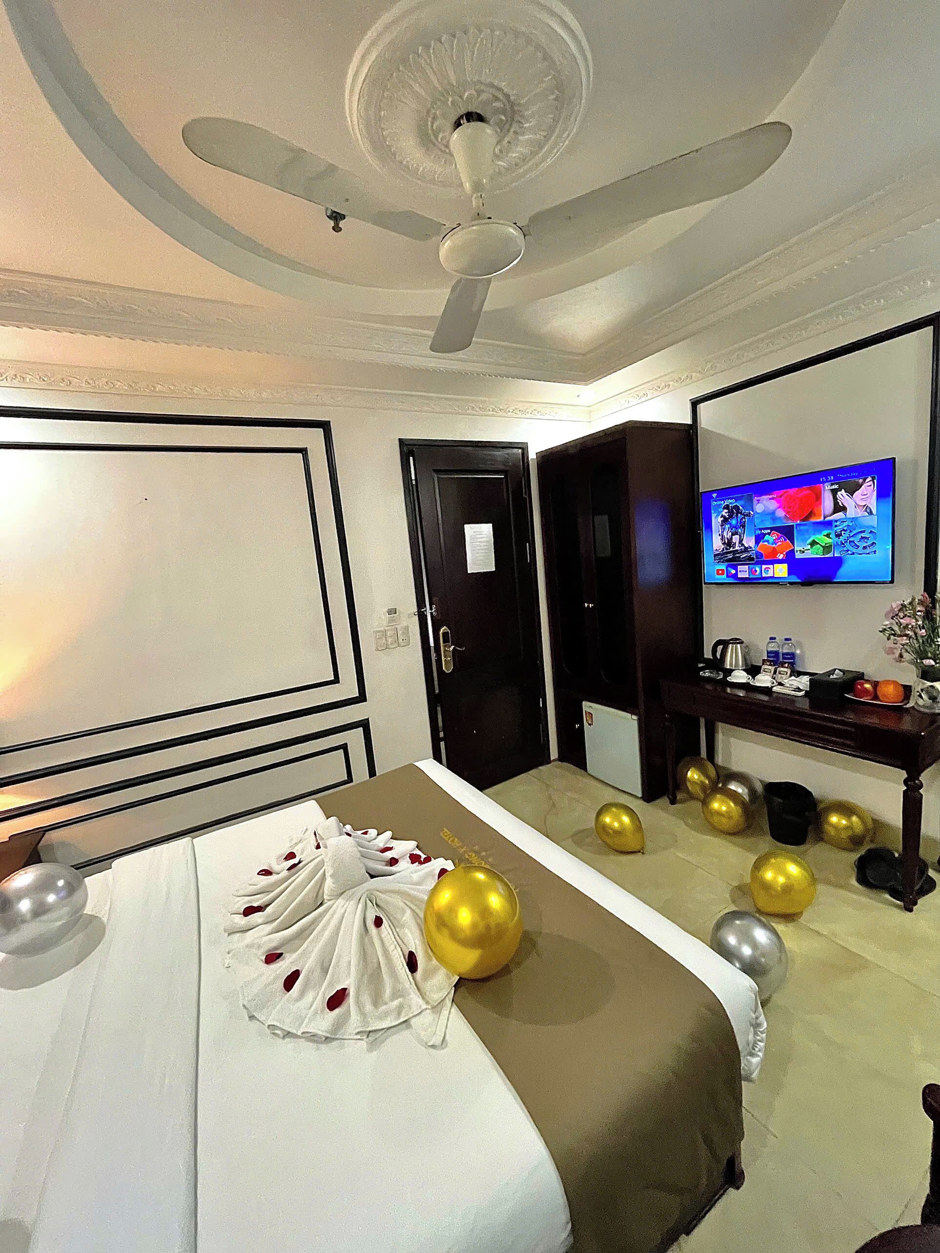 Une chambre d’hôtel équipée d’un lit, d’un ventilateur de plafond, d’une télévision et d’un bureau avec un miroir.