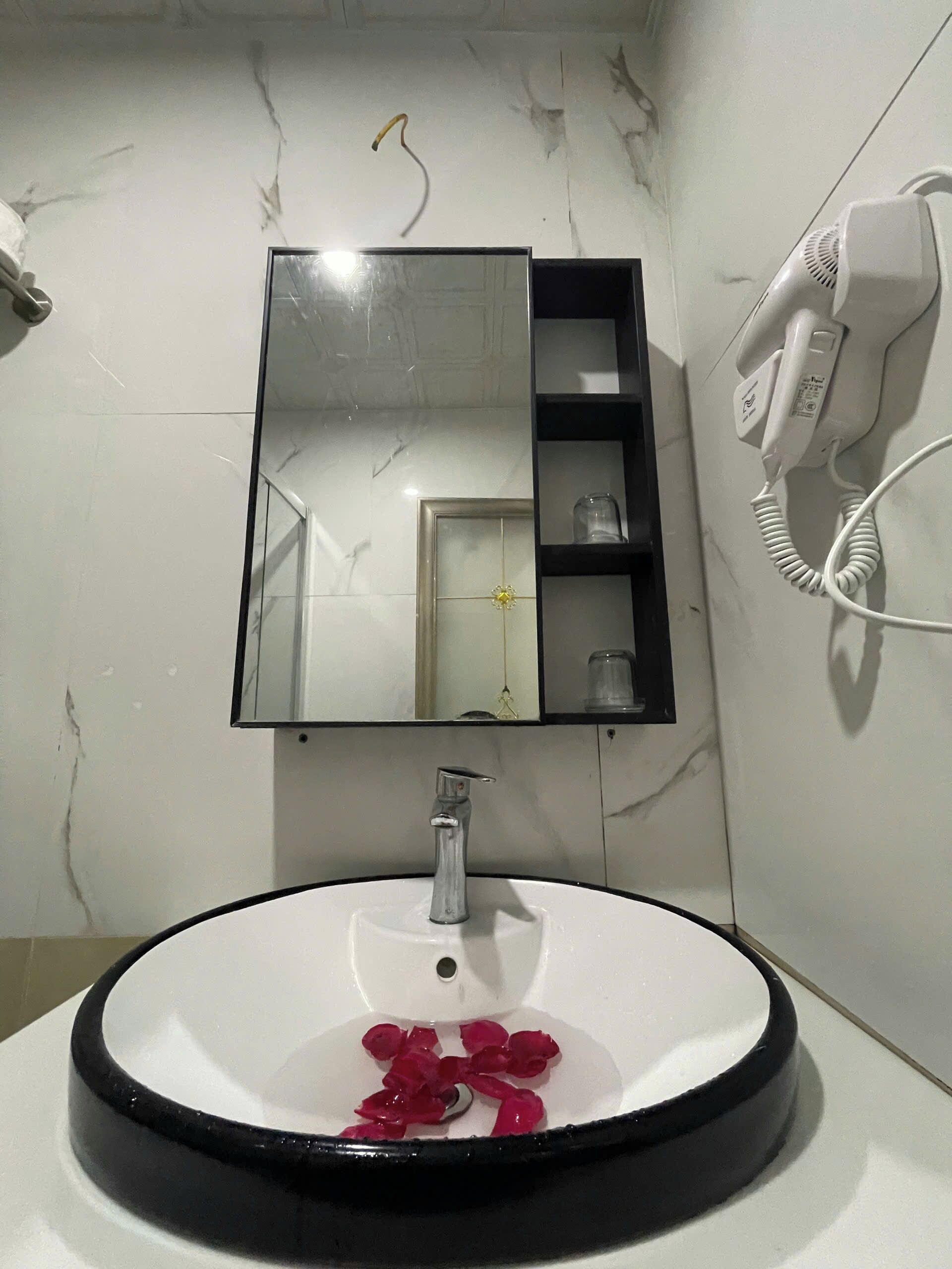 A bathroom with a white sink, a mirror, and a hairdryer mounted on the wall.