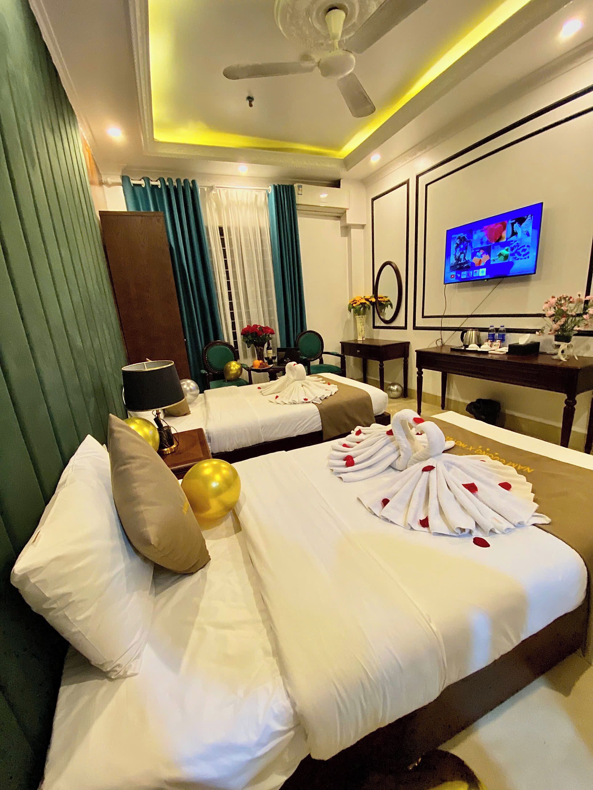 A hotel room with two beds, a ceiling fan, a TV, and a desk with a vase of flowers.