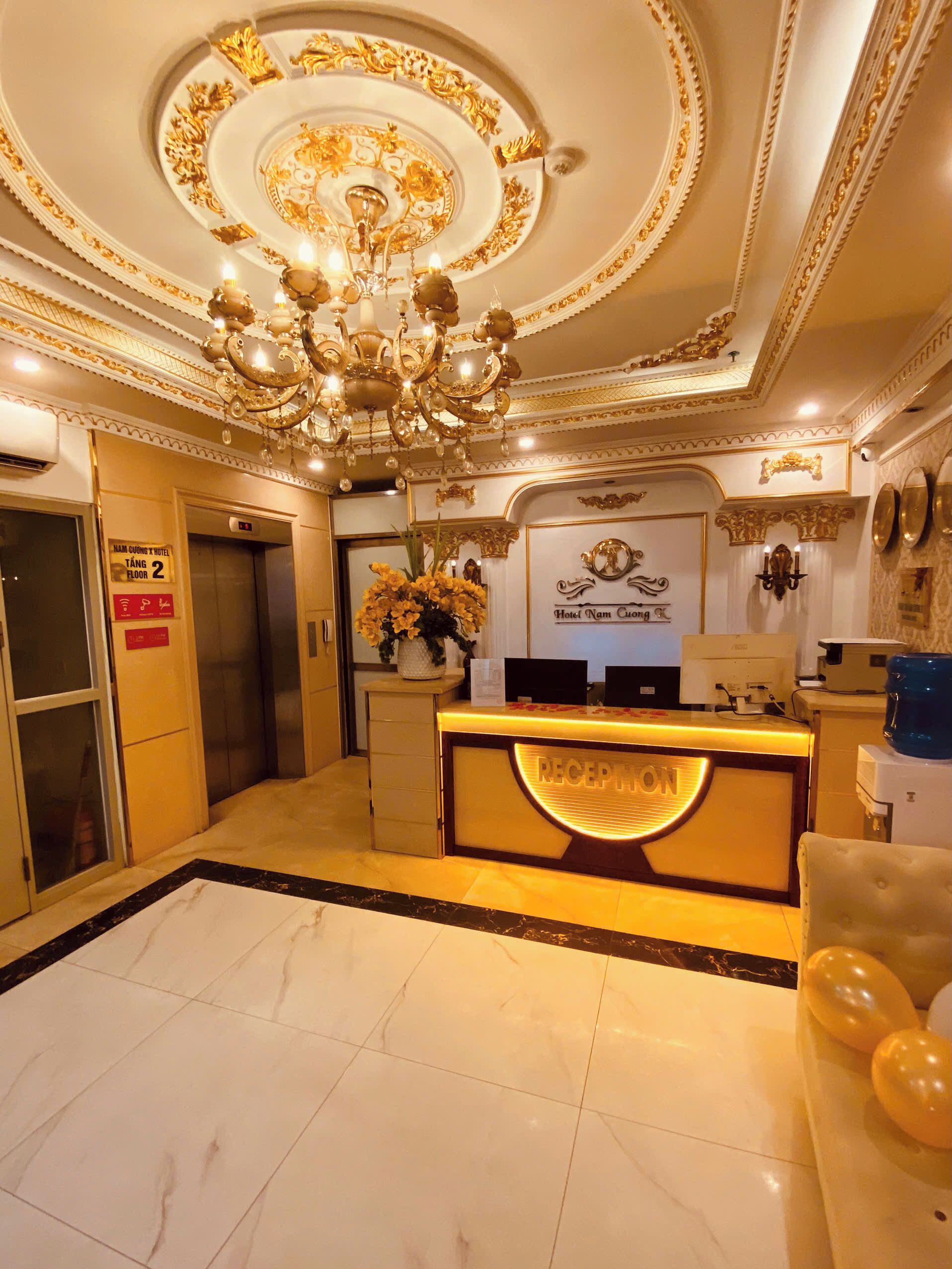 A hotel reception area with a grand chandelier, a reception desk, and an elevator.