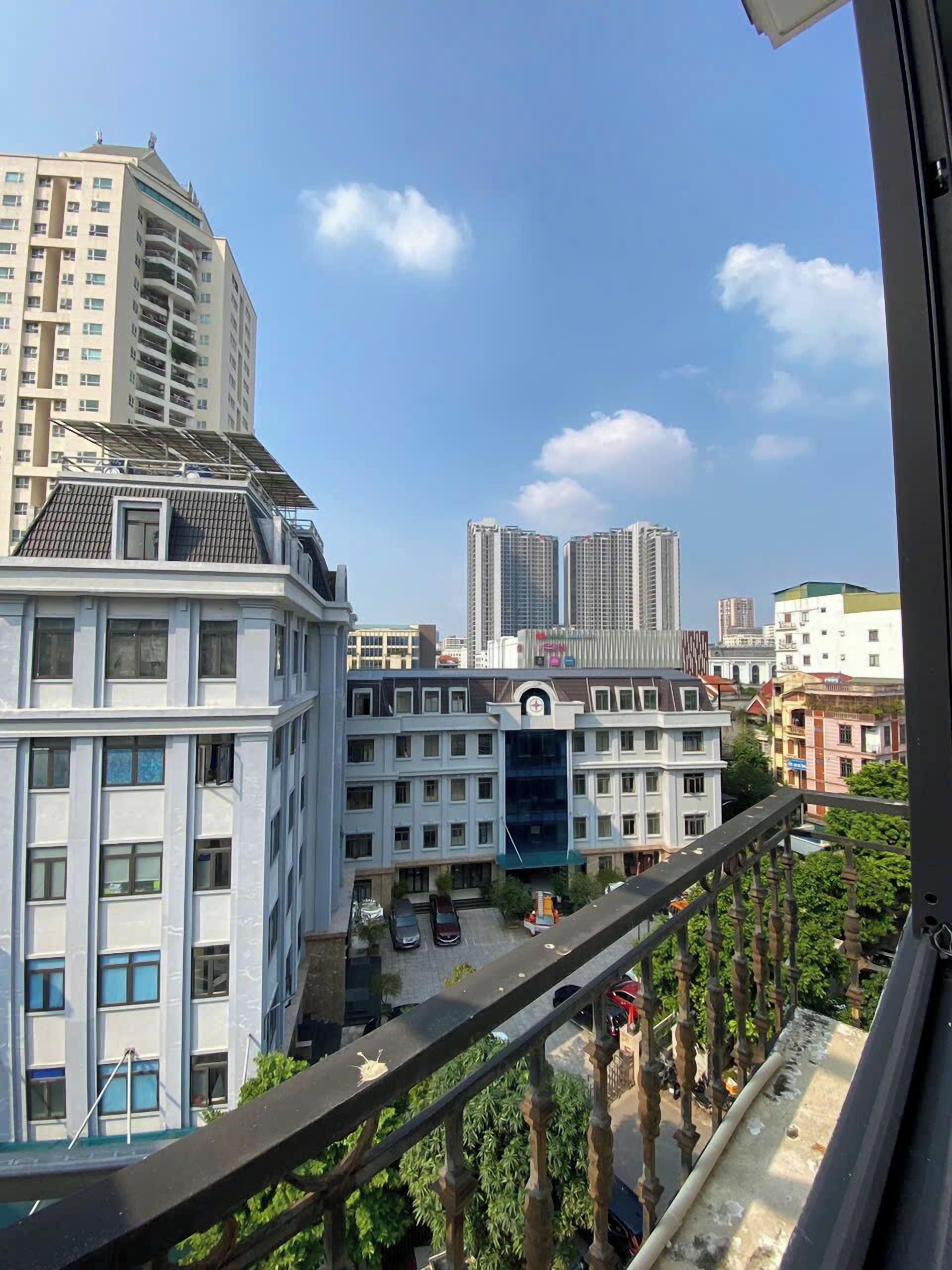 A high-rise building with multiple floors and balconies, surrounded by other buildings and a clear sky.