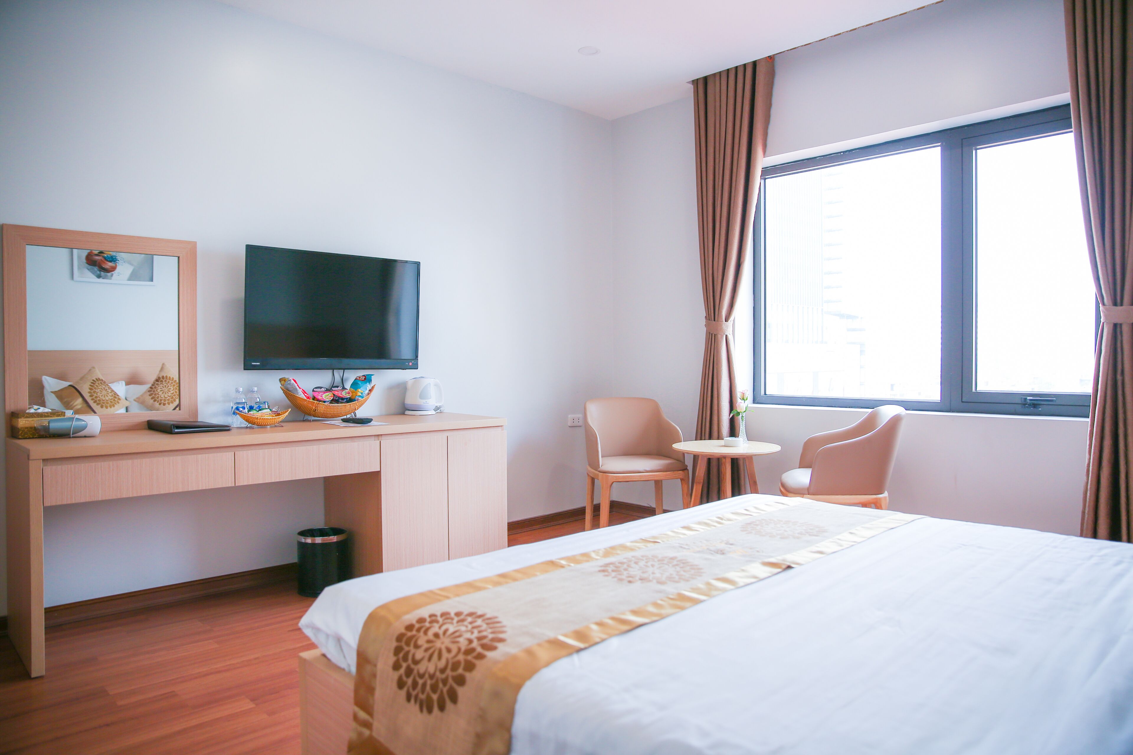 Ein Hotelzimmer mit Bett, Schreibtisch mit Fernseher, Stuhl und einem Fenster mit Vorhängen.