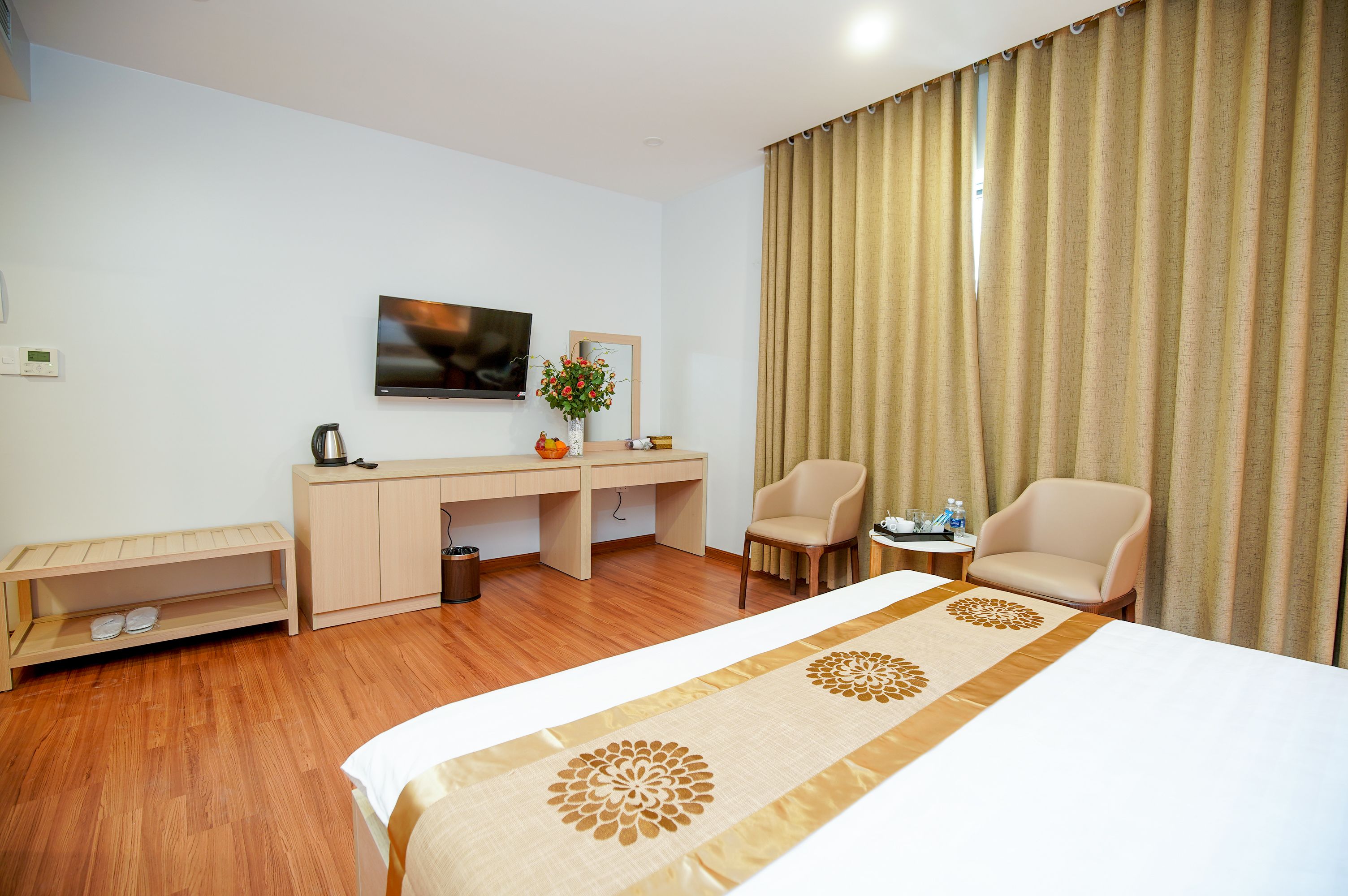 A hotel room with a bed, a desk, two chairs, a TV, and a window with curtains.
