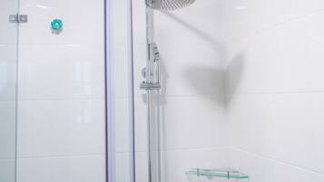 A glass-enclosed shower with a handheld showerhead, a glass shelf, and a tiled wall.