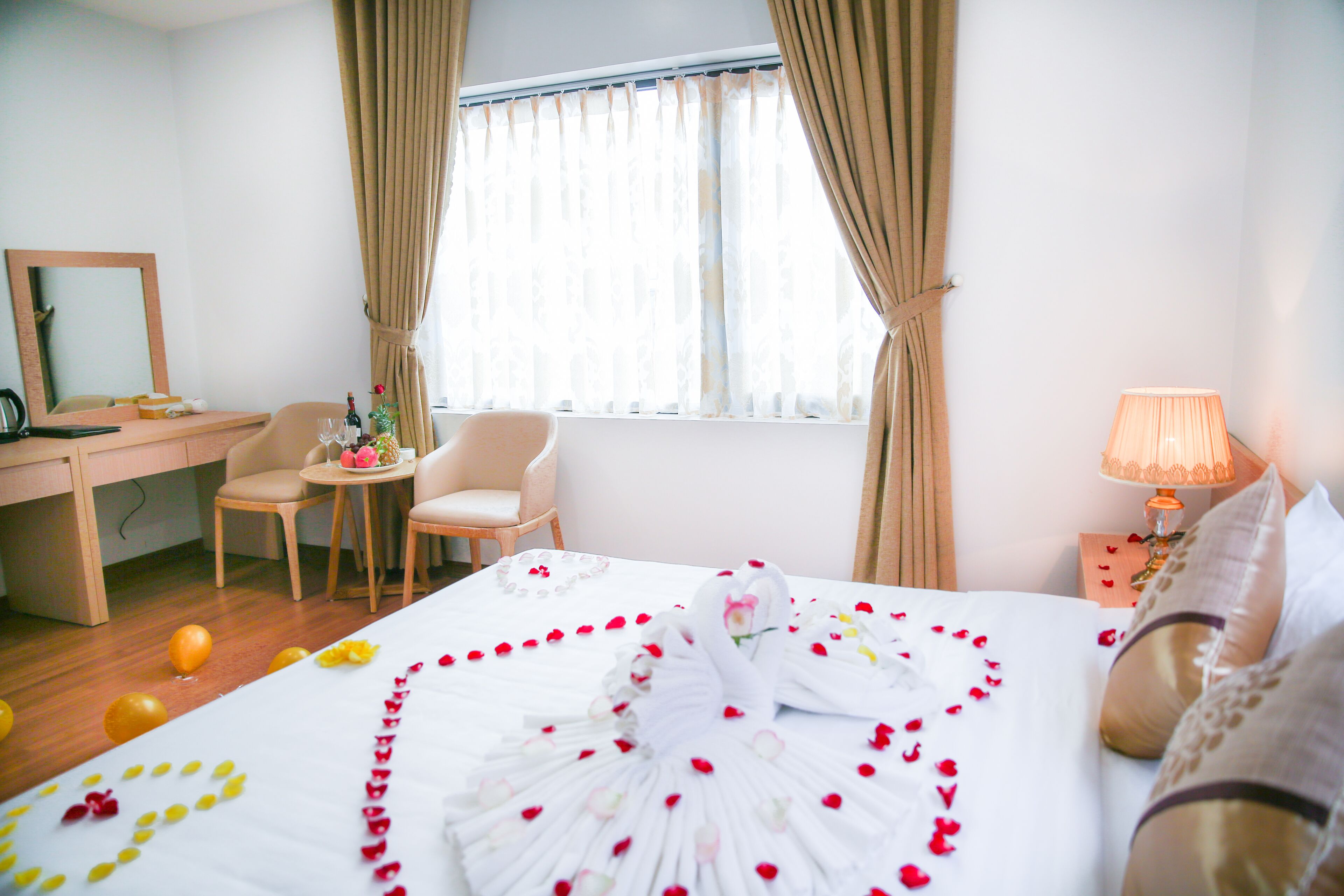 A hotel room with a bed, two chairs, a desk, a lamp, and a window with curtains.