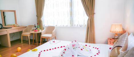 A hotel room with a bed, two chairs, a desk, a lamp, and a window with curtains.