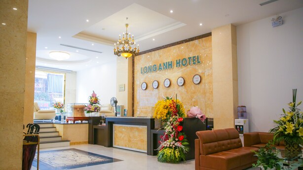 Zona de recepción de un hotel con pared de mármol, una araña, mostrador de recepción, un sofá y un gran arreglo floral.