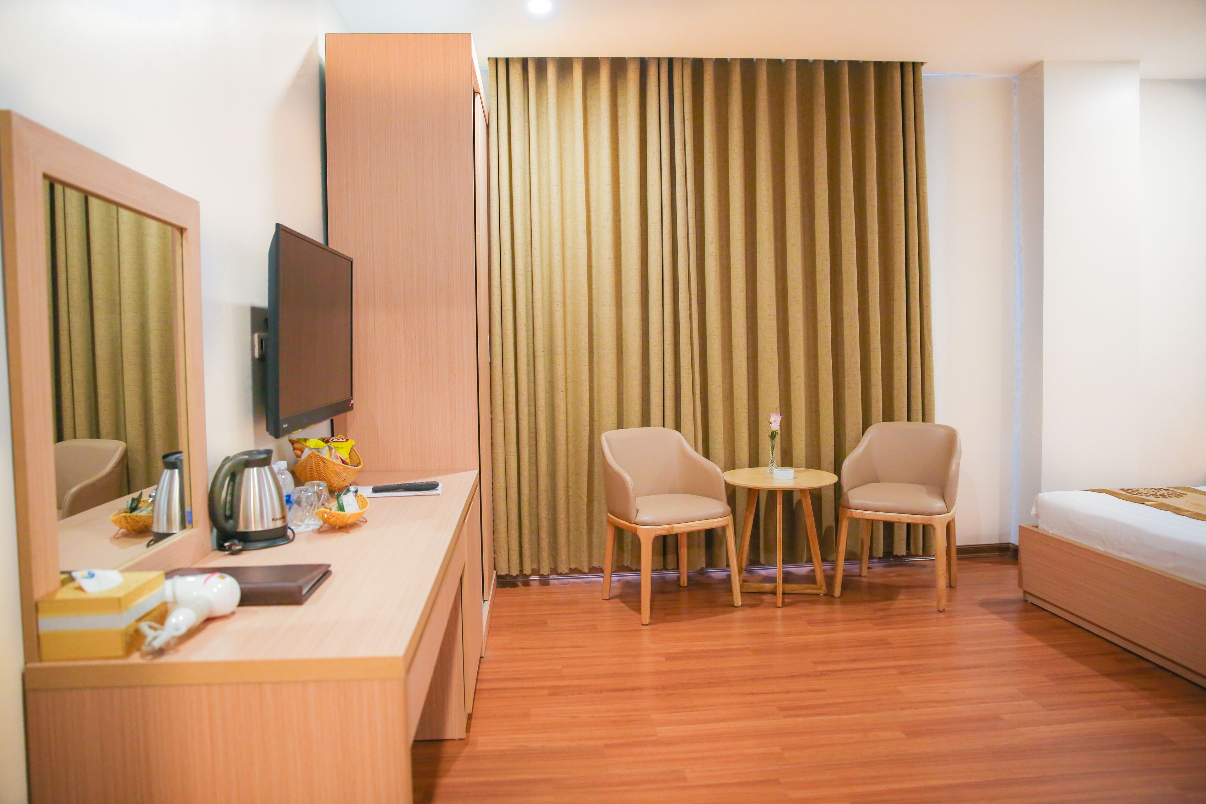 Una habitación de hotel con un escritorio de madera, un televisor, dos sillas, una mesita y una cama.