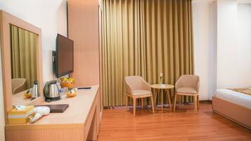 A hotel room with a wooden desk, a television, two chairs, a small table, and a bed.