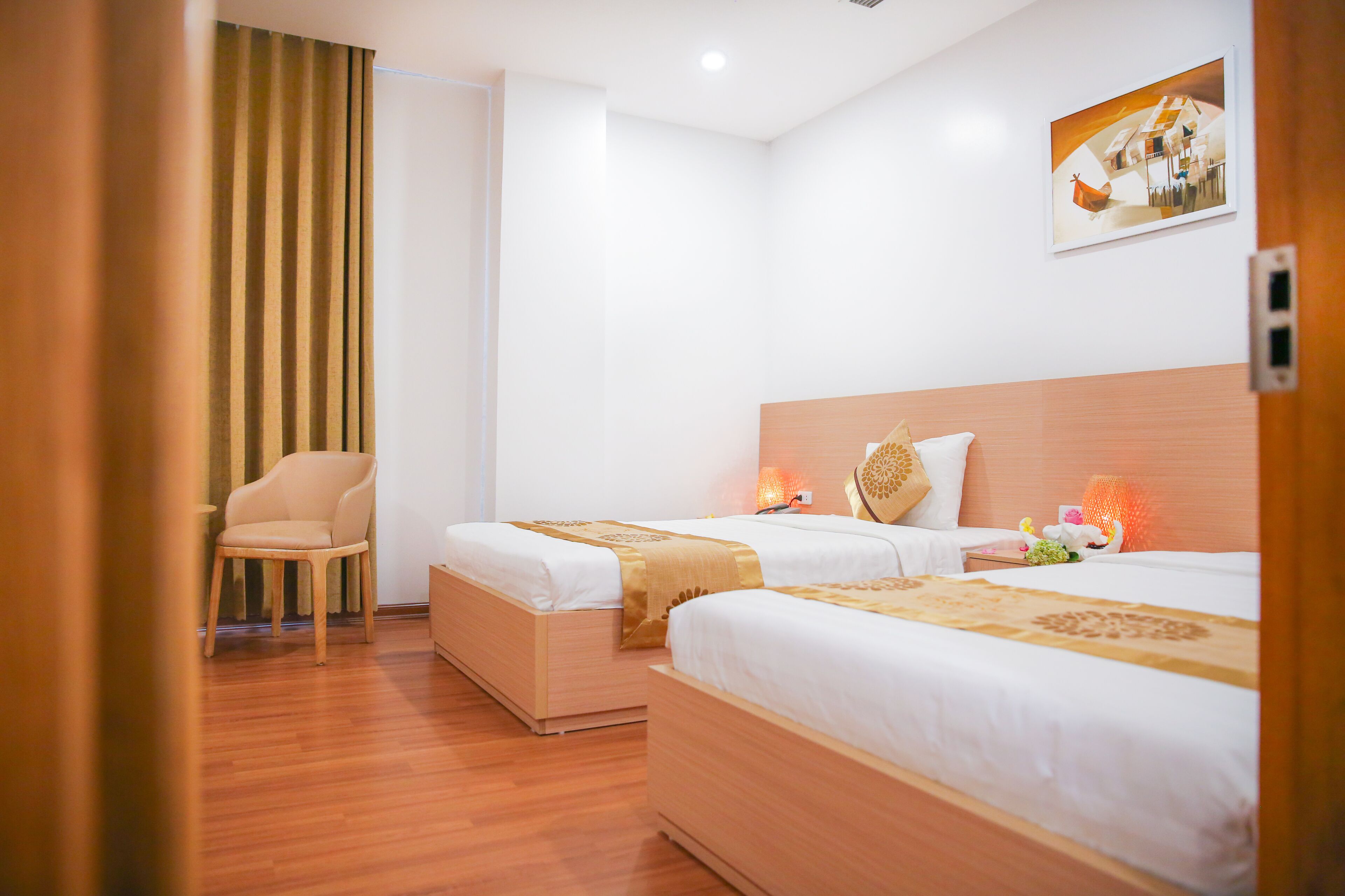 Habitación de hotel con dos camas, piso de madera, una silla y un cuadro en la pared.