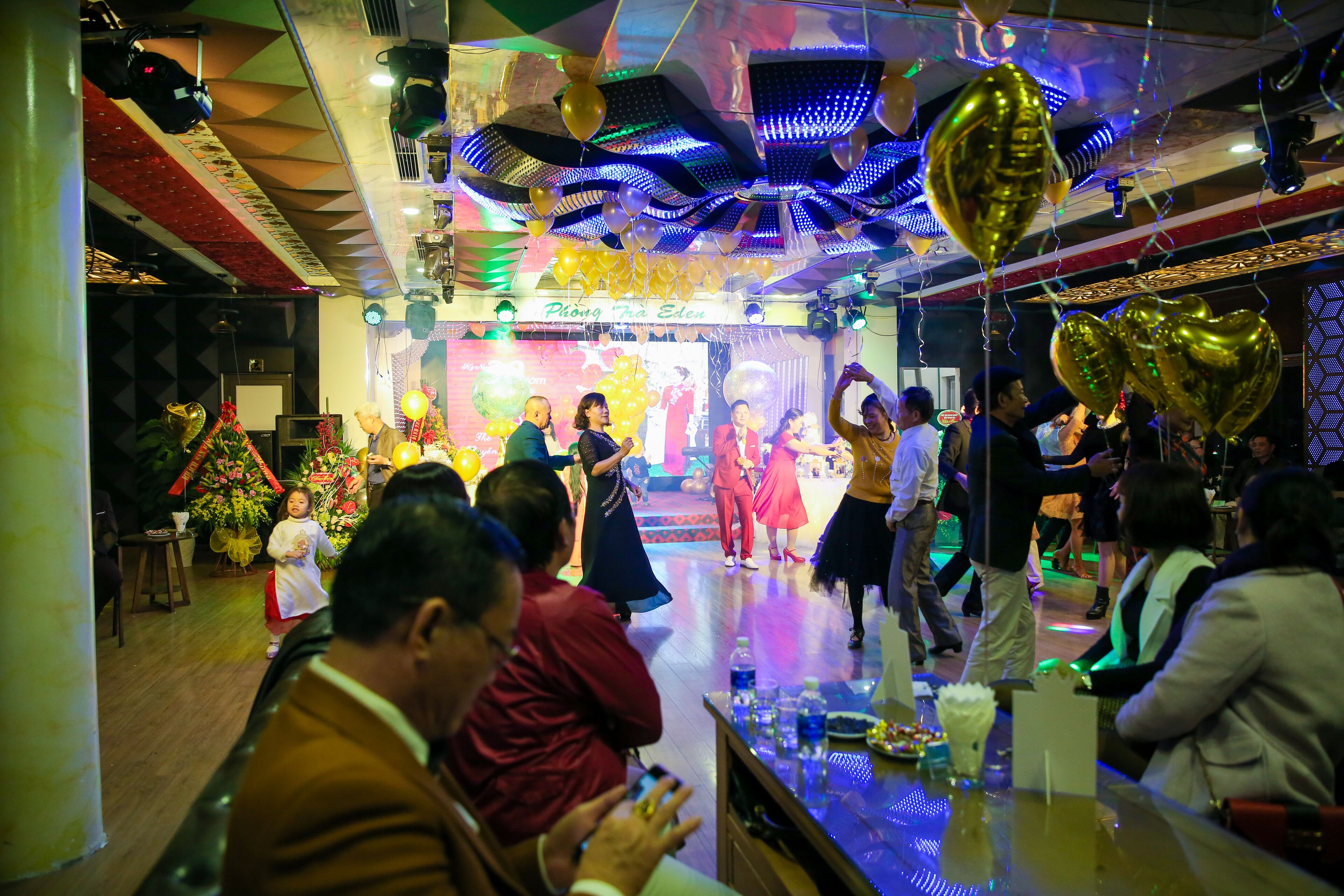 Een feestelijk evenement in een ruimte, met een podium, ballonnen en gasten.