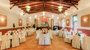 Un salón de banquetes con suelos de madera, mesas blancas con manteles rojo y blanco y sillas blancas adornadas con cintas rojas.