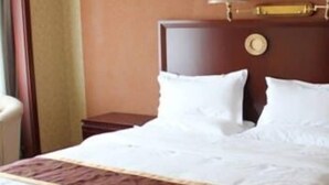 A hotel room with a large bed, a nightstand, a lamp, and a wall clock. - Balin Hotel (Chifeng)