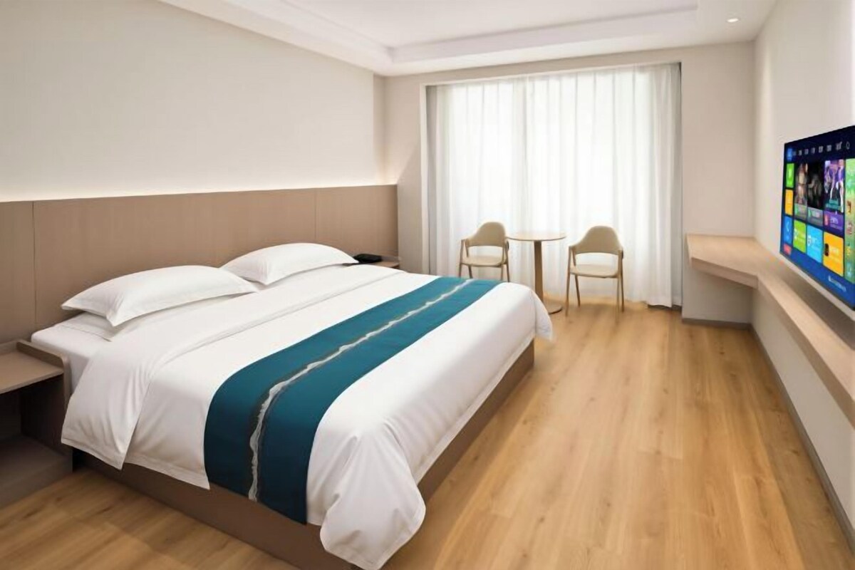 A hotel room with a bed, a desk, a chair, and a window with curtains.