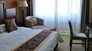 A hotel room with a large bed, a desk, a chair, and a lamp. - Balin Hotel (Chifeng)