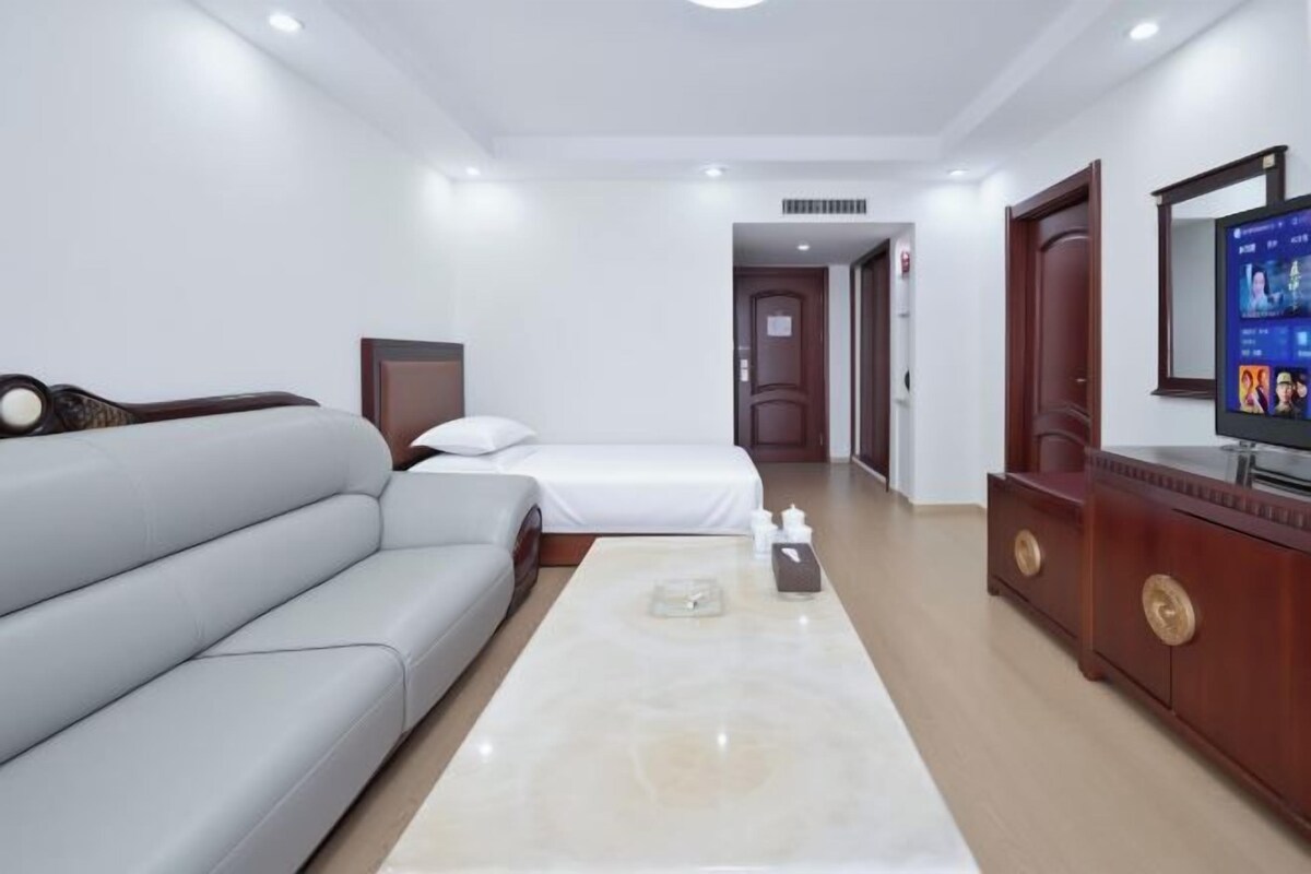 A hotel room with a sofa, a bed, a TV, and a wooden cabinet.