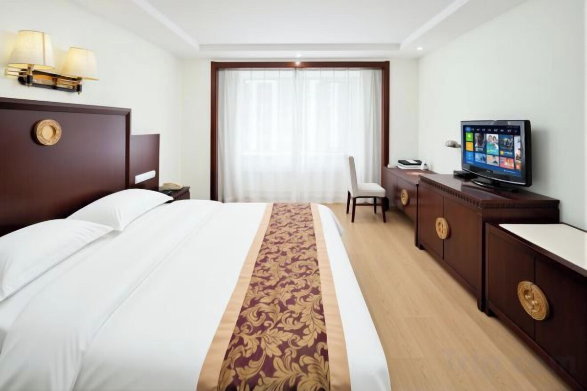 A hotel room with a large bed, a desk with a television, and a window with curtains.