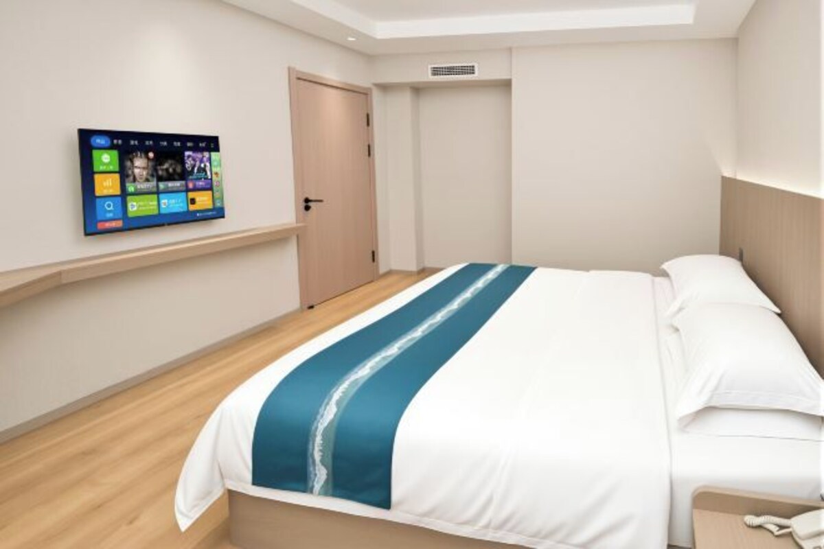 A hotel room with a bed, a television mounted on the wall, and a door.