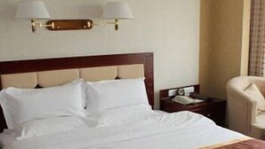 A hotel room with a large bed, a bedside table, a chair, and a lamp. - Balin Hotel (Chifeng)